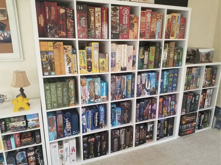 a book shelf filled with lots of books on top of carpeted floor next to a lamp