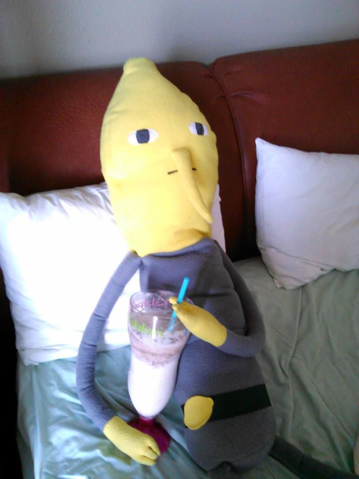 a stuffed banana sitting on top of a bed with a drink in it's hand