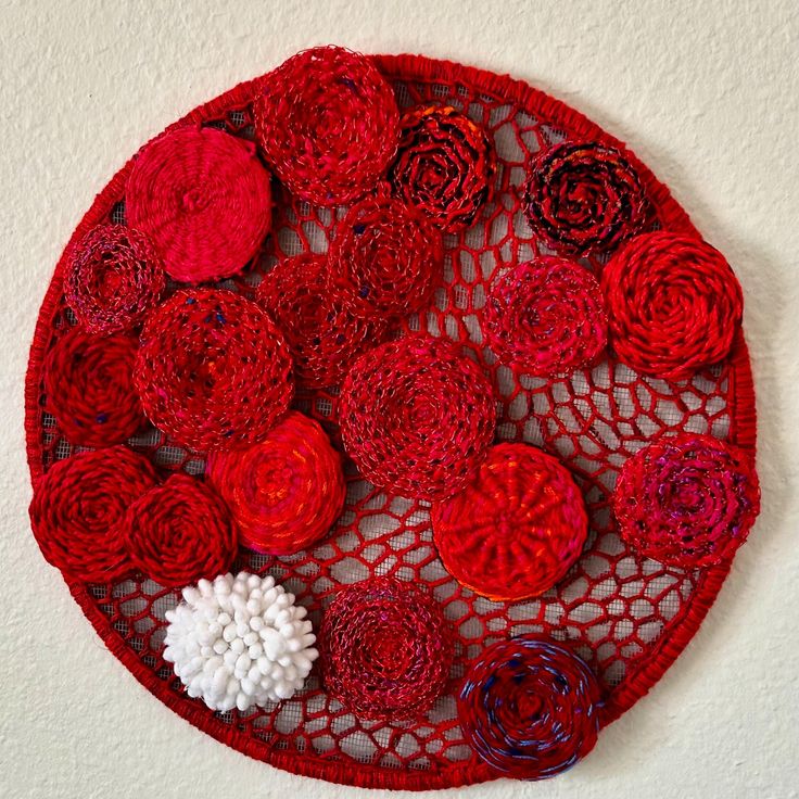 a red doily with crocheted flowers on it is hanging on the wall