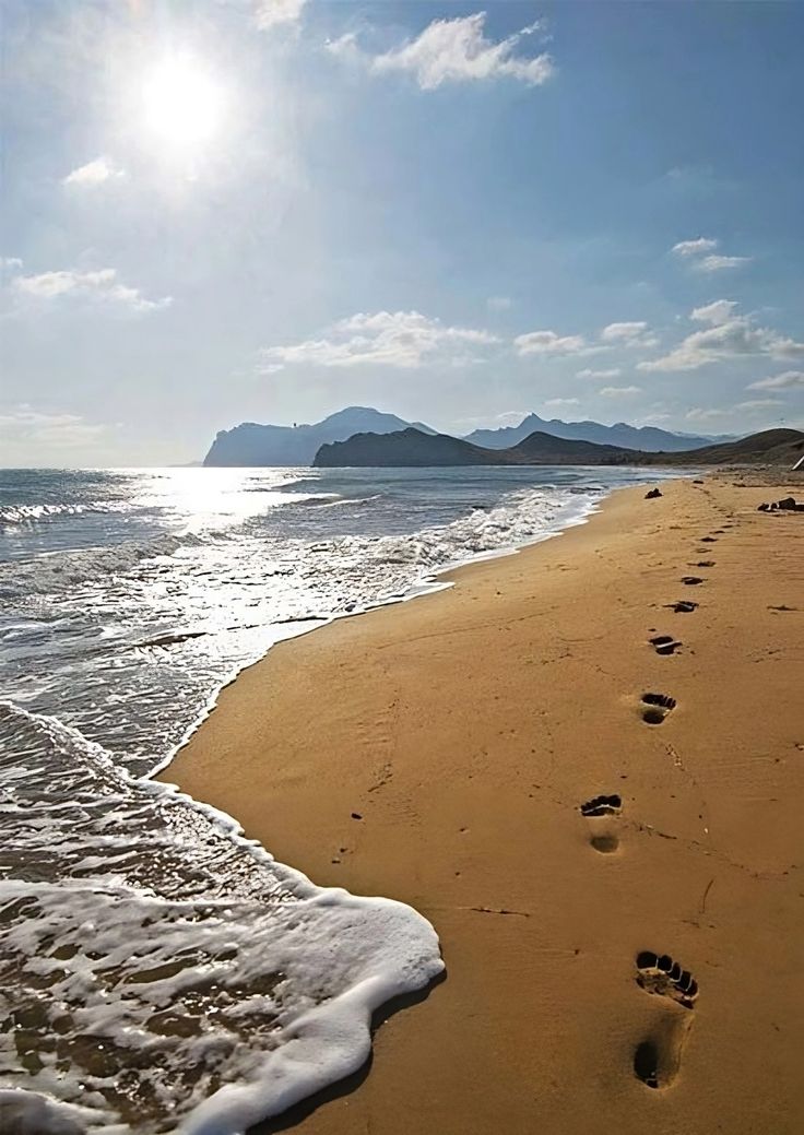 footprints in the sand at the beach with mountains in the background