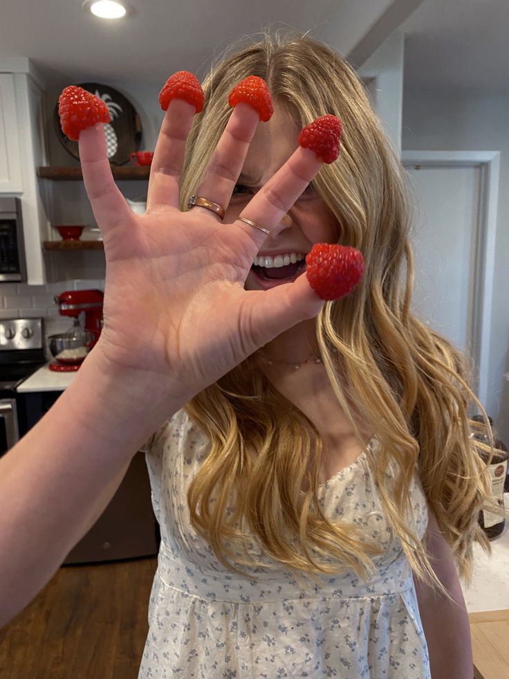 a woman with long blonde hair holding up two raspberries in front of her face