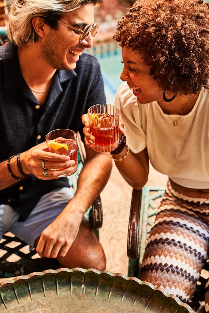 a man and woman sitting next to each other holding glasses in their hands while laughing