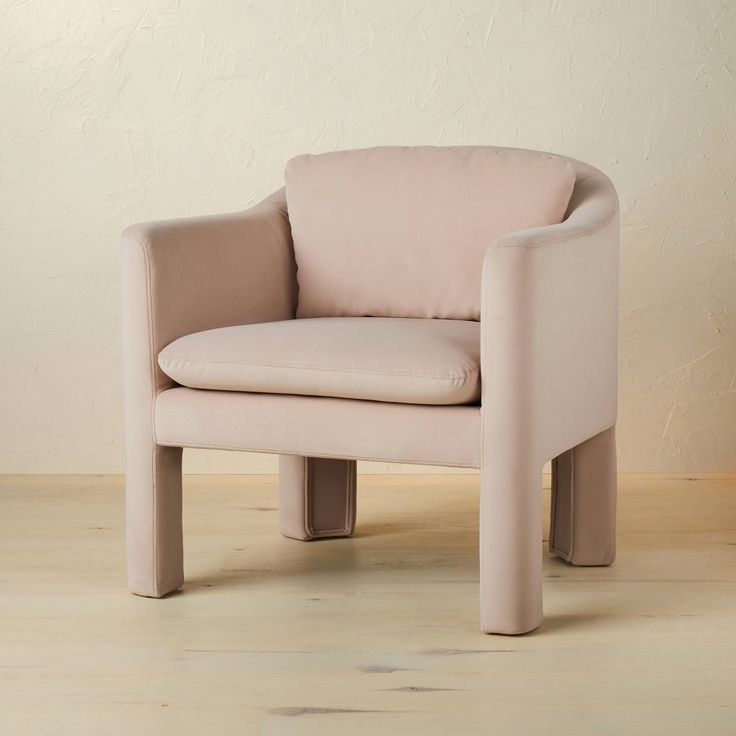 a pink chair sitting on top of a hard wood floor next to a white wall