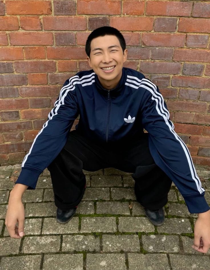 a man is posing for the camera in front of a brick wall with his hands on his knees