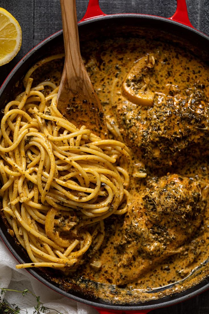 a skillet filled with pasta and chicken covered in parmesan cheese sauce next to sliced lemon wedges