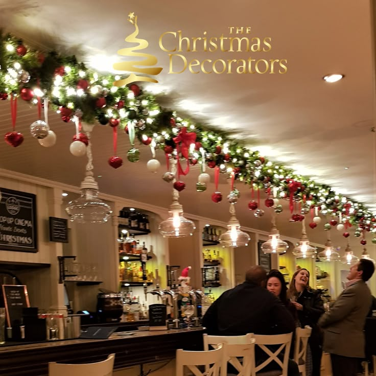 people sitting at tables in a restaurant with christmas decorations hanging from the ceiling