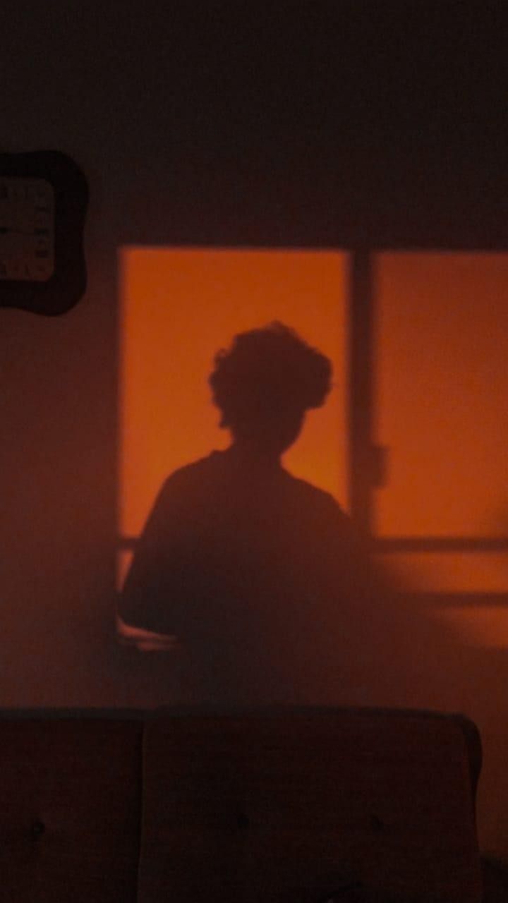 the shadow of a person sitting in front of a window with an orange glow on it