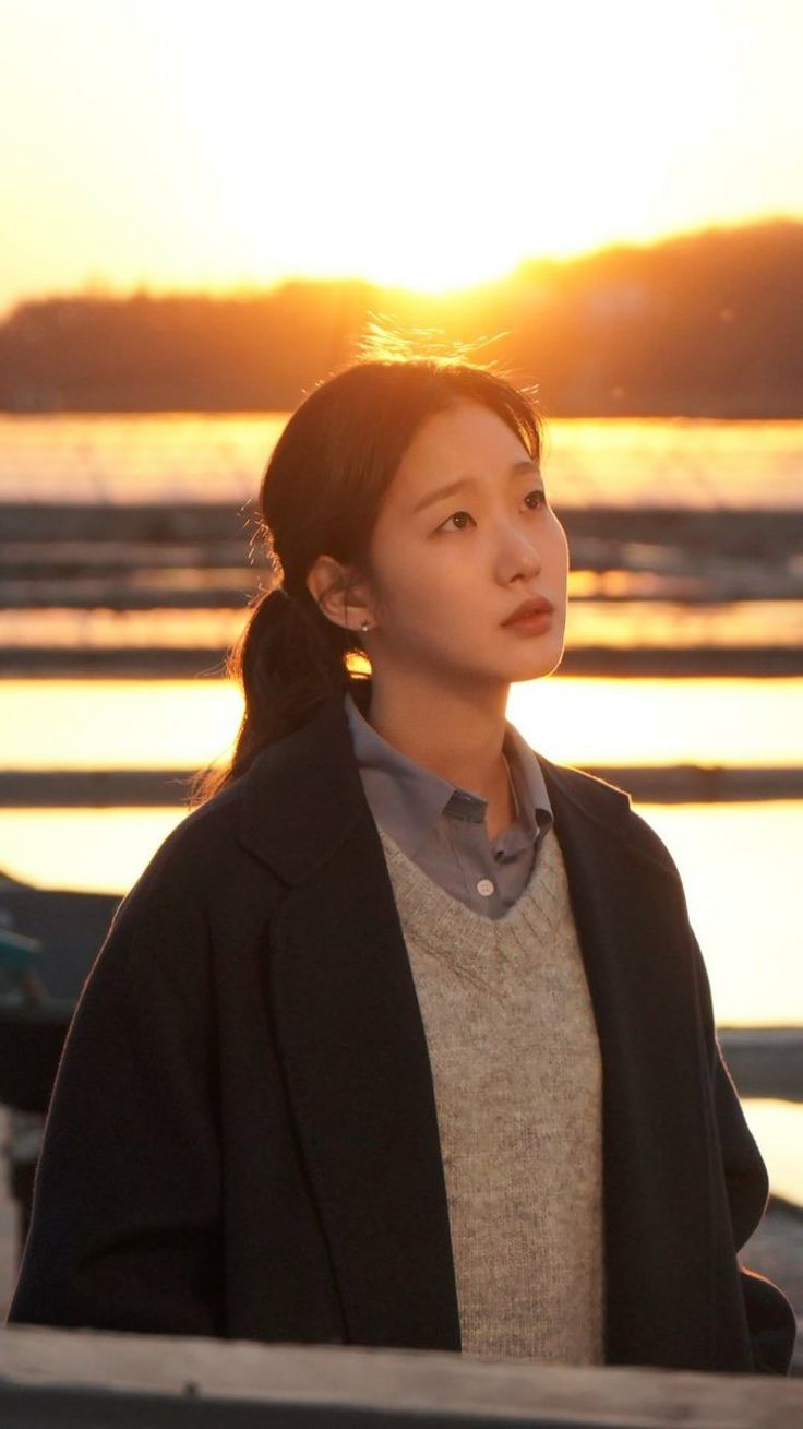 a woman standing next to the water at sunset