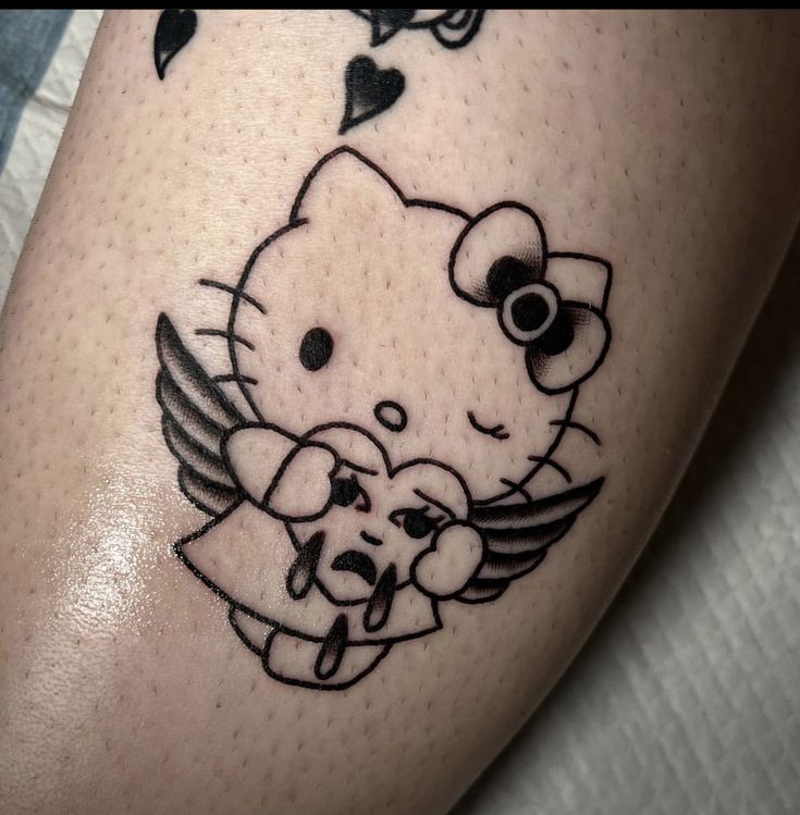 a hello kitty tattoo on the leg of a woman with an angel wing and heart