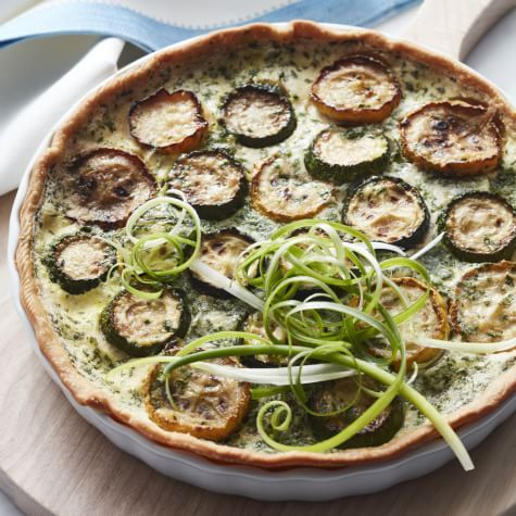 a quiche with zucchini and onions on a wooden board next to utensils