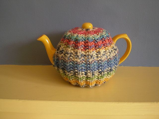 a knitted tea pot cover sitting on top of a wooden table next to a wall