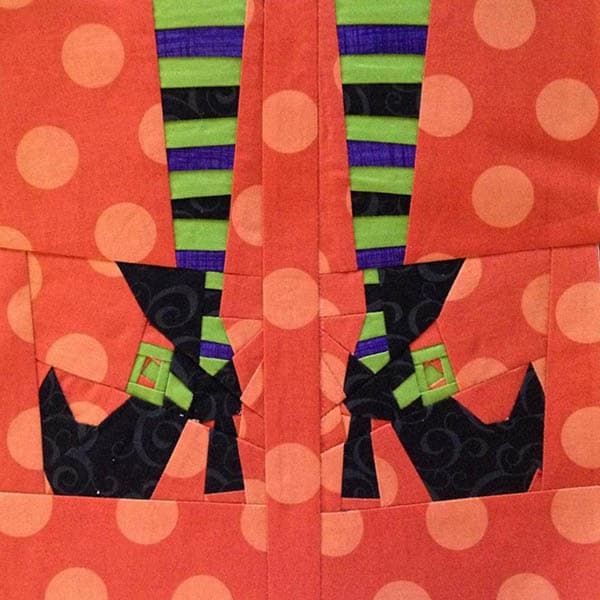 an orange and black quilted piece with two legs in the shape of a witch's boot