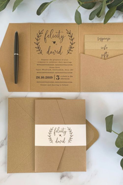 the wedding stationery is laid out on top of brown envelopes, with a pen next to it