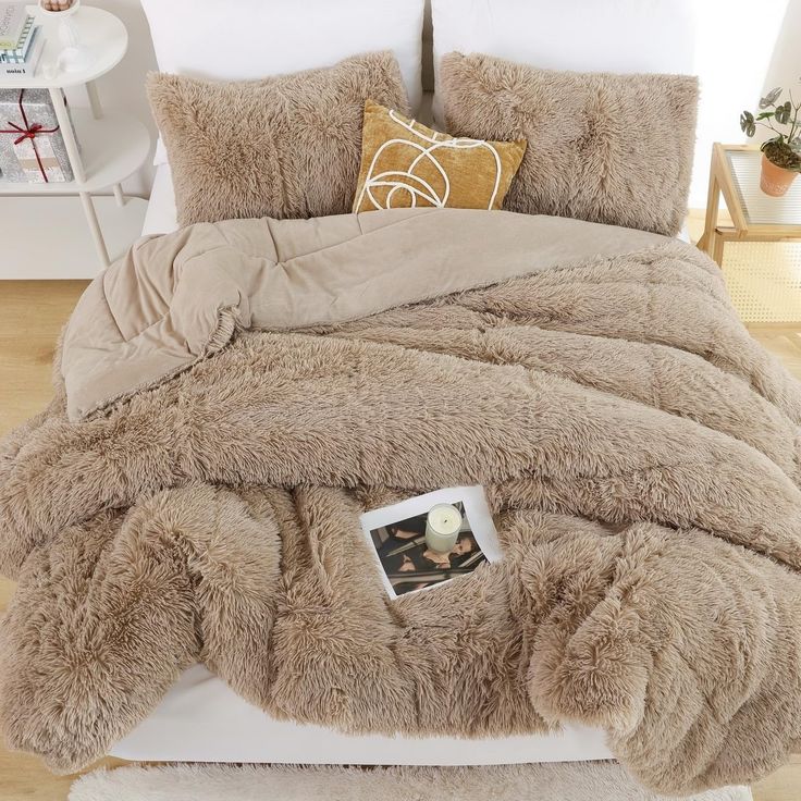 a bed covered in a fluffy brown comforter and pillows with pictures on the pillow