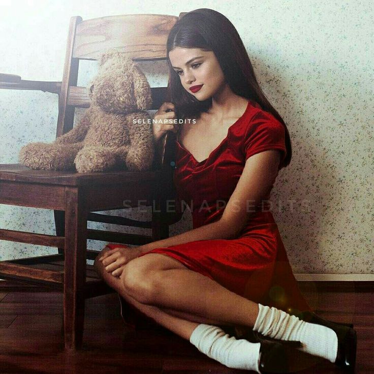 a woman in a red dress sitting on a wooden chair with a teddy bear next to her