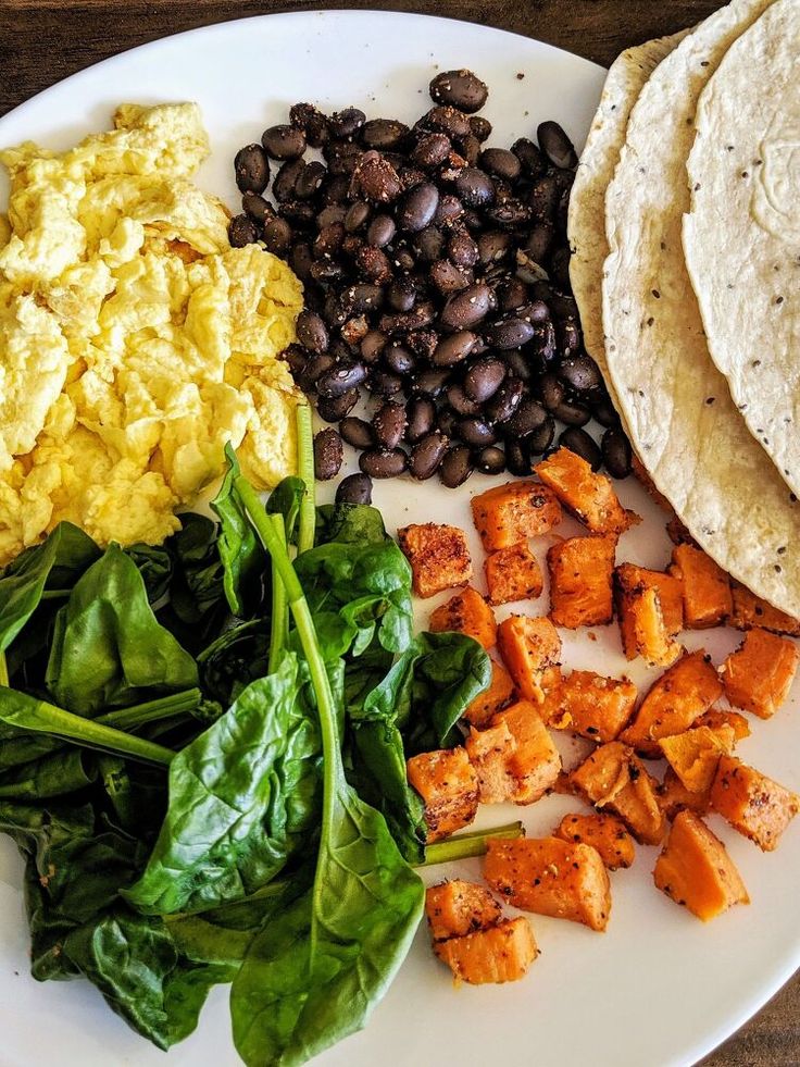 a plate with eggs, spinach, and sweet potato salad on it next to tortillas