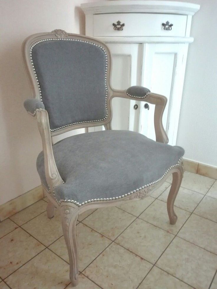 an old chair is upholstered in grey fabric and sits on the tiled floor