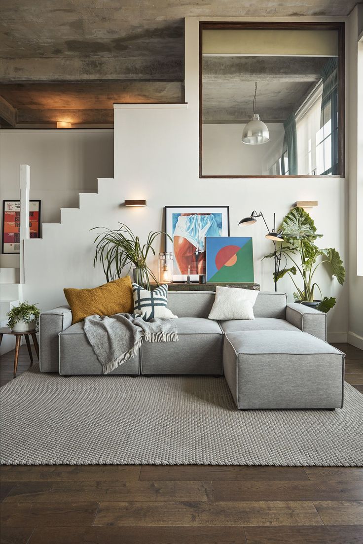 a living room filled with lots of furniture next to a window covered in plants and paintings