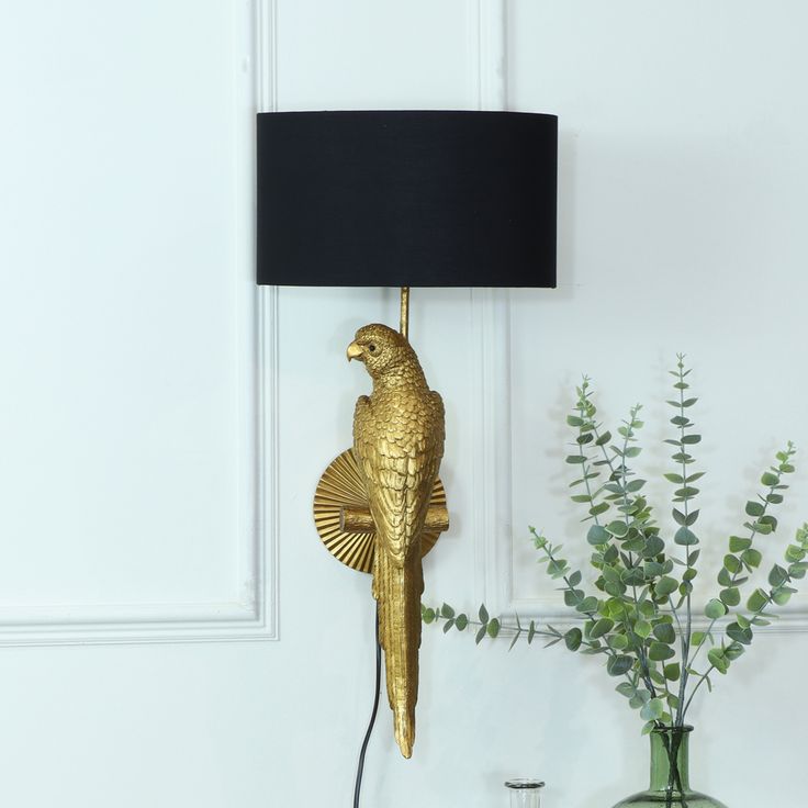 a gold parrot lamp on a white wall next to a vase with flowers and greenery