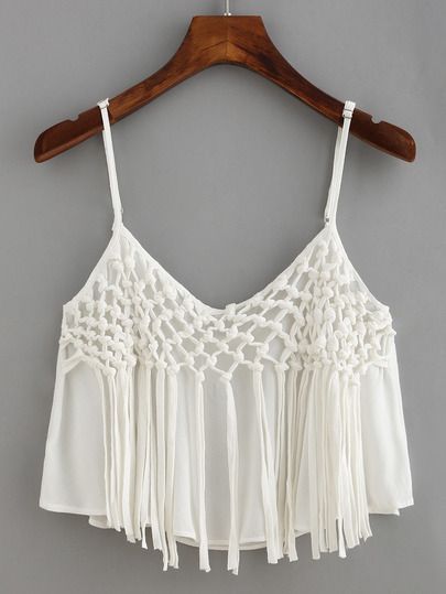 a crop top with tassels hanging on a hanger against a gray wall