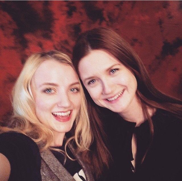 two women taking a selfie in front of a red background