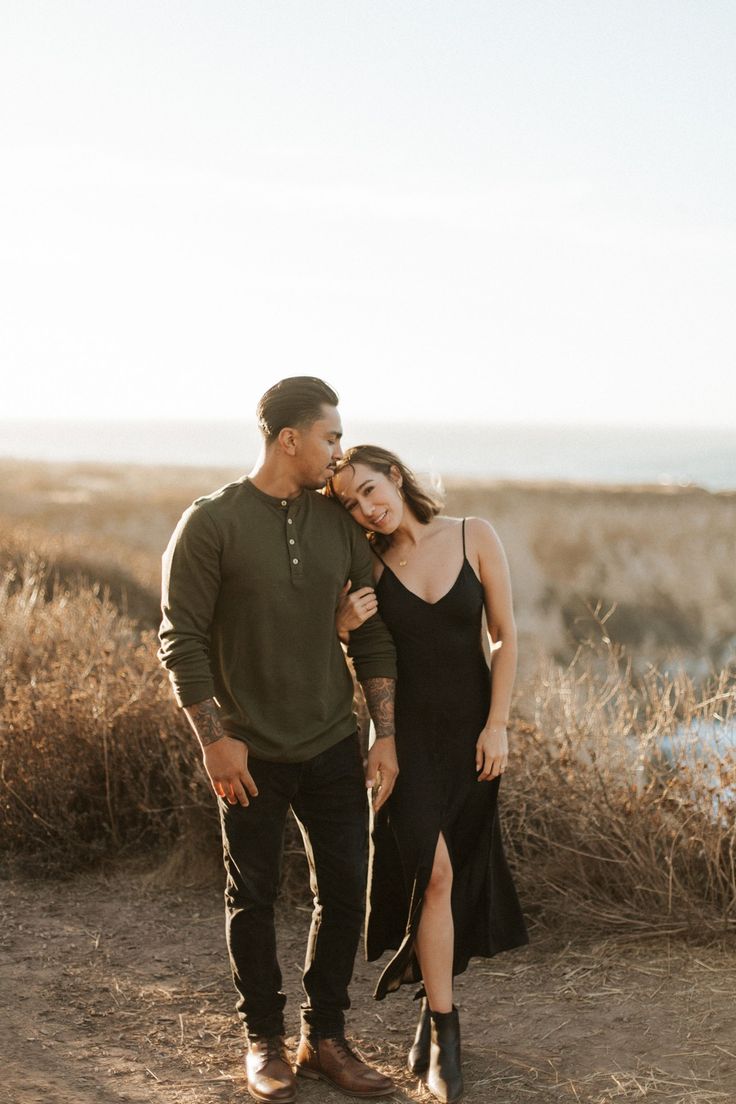 a man and woman standing next to each other in front of some tall brown grass