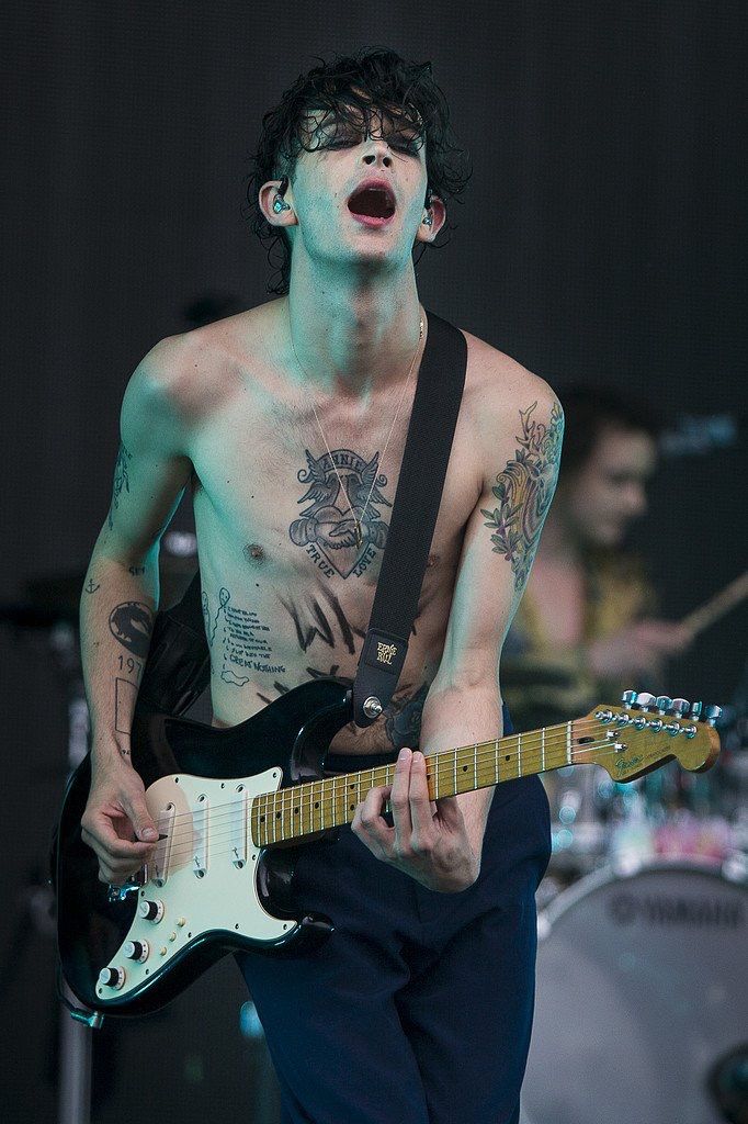 a shirtless man playing an electric guitar on stage