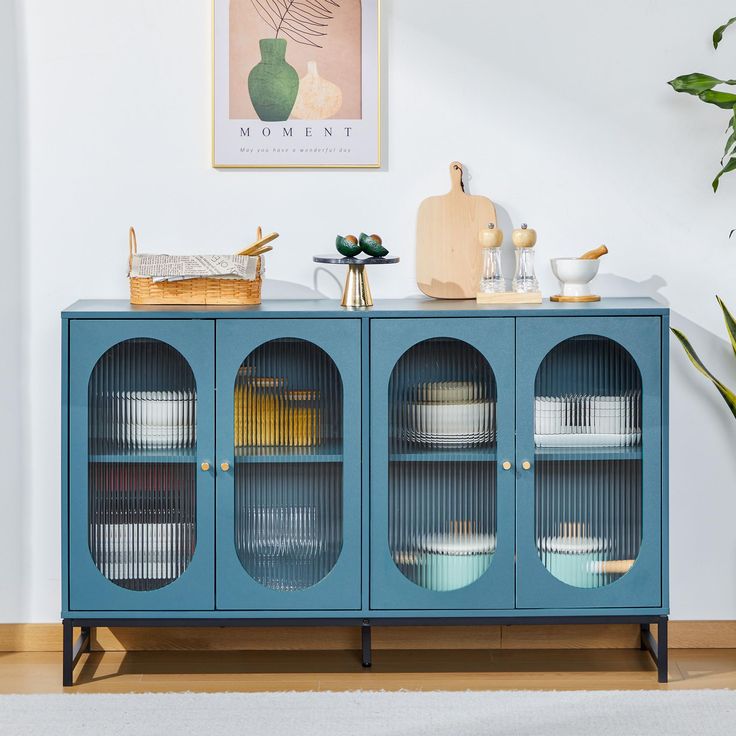 a blue cabinet with glass doors and plates on it in front of a wall mounted art piece