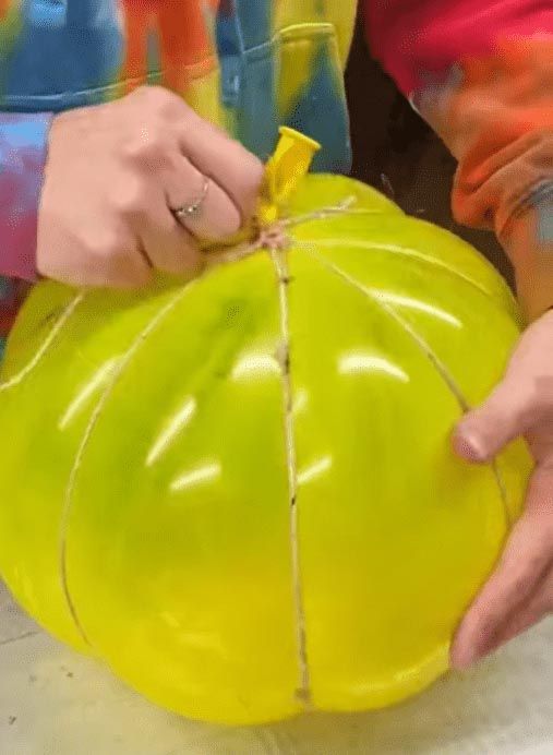 a person holding a large yellow object in their hands and wrapping it around with string