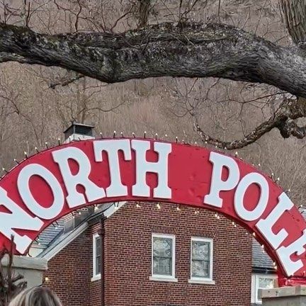 a red sign that says north pole on the side of a brick building in front of a tree