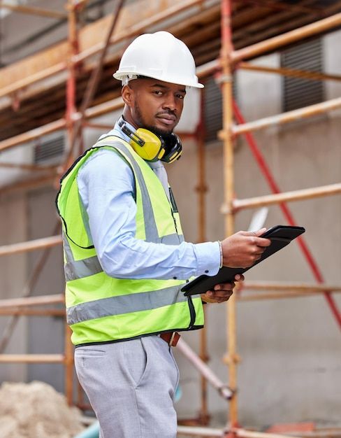 a construction worker wearing a safety vest and ear muffs looking at something on his tablet