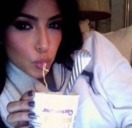 a woman is drinking out of a cup while laying on a bed with her tongue hanging out