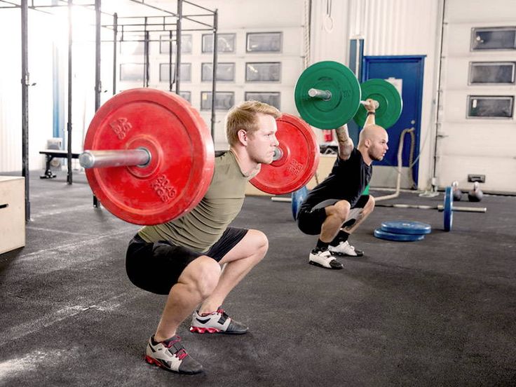 two men doing squats with red and green barbells