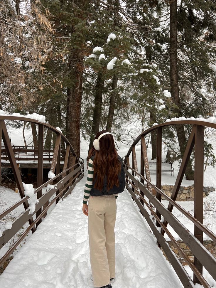 a woman standing on a bridge in the snow with her back turned to the camera