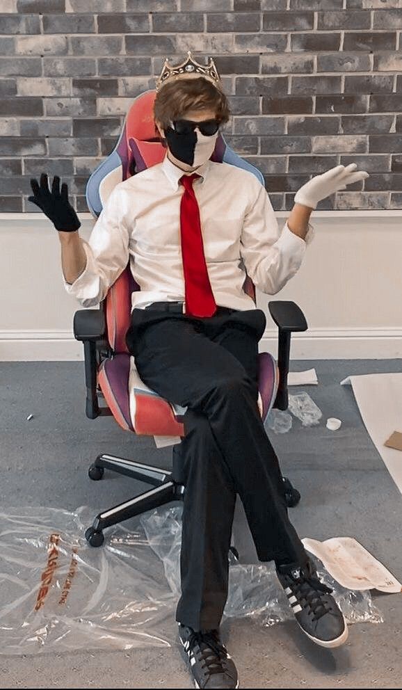 a man in a suit and tie sitting on a chair with his hands up while wearing a mask