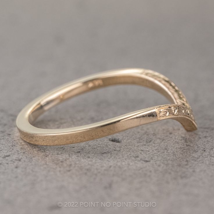 a yellow gold wedding band with an intricate design on the top and bottom, sitting on a gray surface