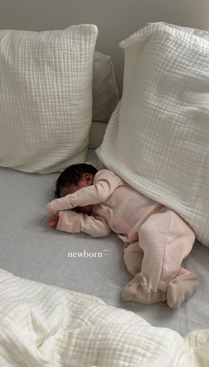 a baby laying on top of a bed next to pillows