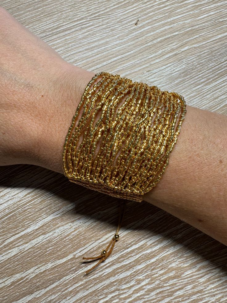 a woman's arm with gold colored bracelets on top of wooden table next to scissors