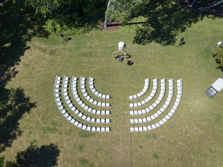 an aerial view of rows of white chairs in the middle of a grassy area with trees