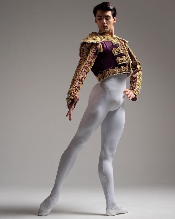 a male ballet dancer in white tights and an elaborate gold jacket is posing for the camera