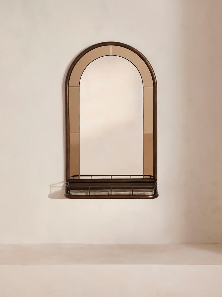 an arched window on the side of a white wall next to a shelf with a mirror