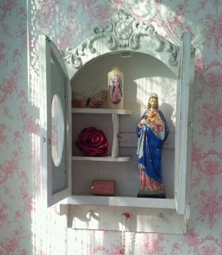 a small shrine in the corner of a pink and white wallpapered room,