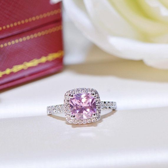 a pink diamond ring sitting on top of a white table next to a red box