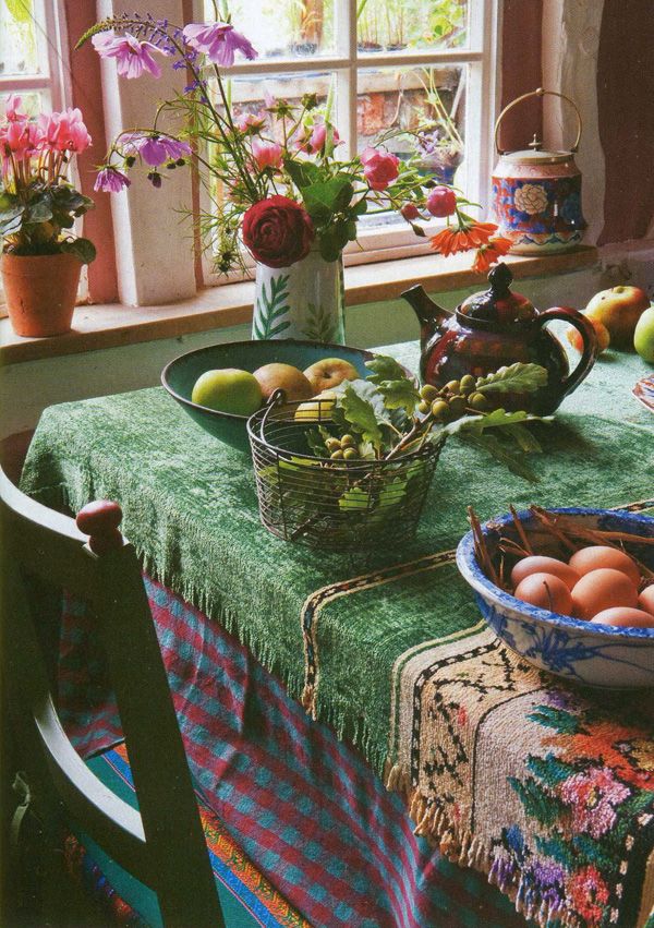 a table with flowers, fruit and eggs on it in front of a windowsill