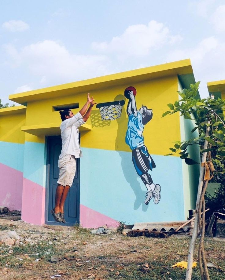 a man is painting a mural on the side of a building with a basketball hoop