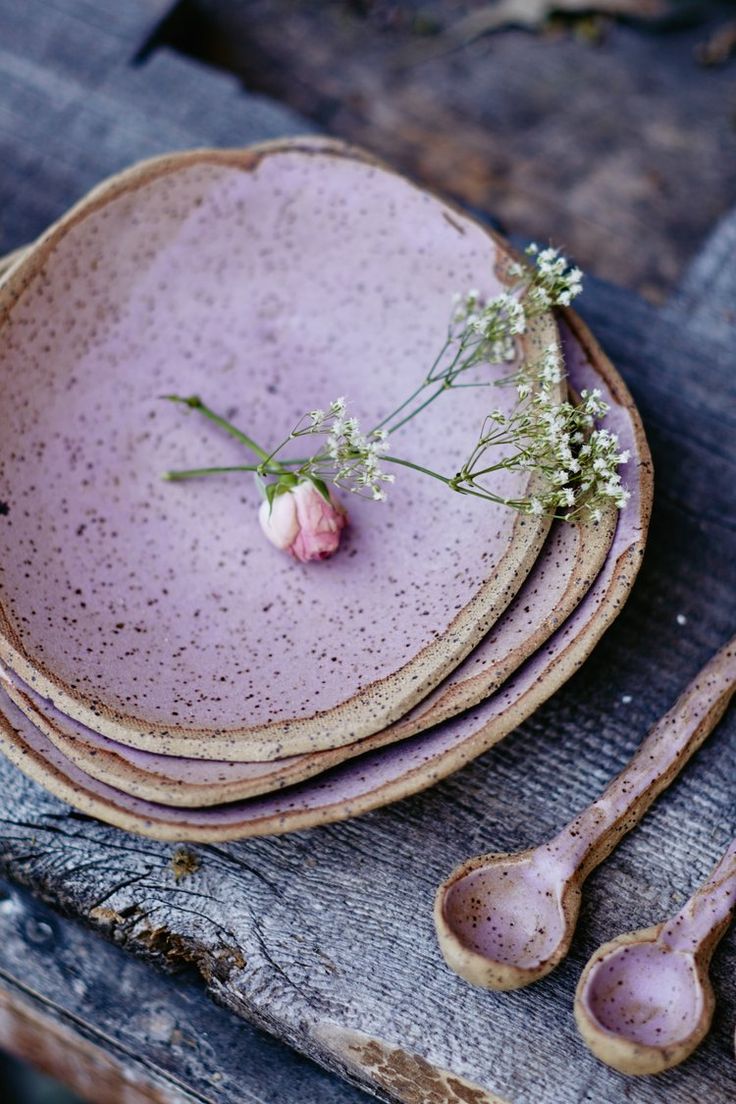 purple dishes with spoons and flowers sit on a wooden table top, ready to be used as place settings