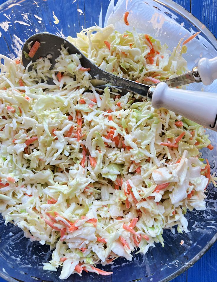 a bowl filled with coleslaw and carrots next to a pair of tongs