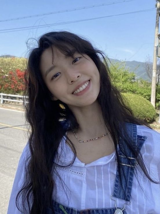 a woman with long black hair standing on the side of a road smiling at the camera