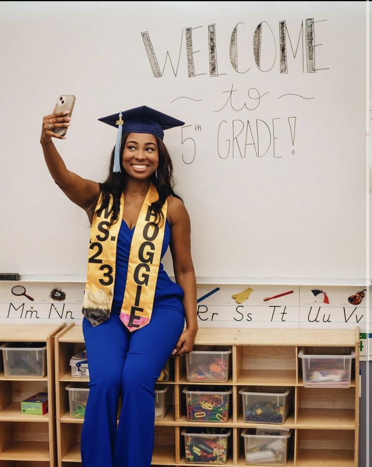 a woman wearing a graduation cap and gown posing in front of a whiteboard