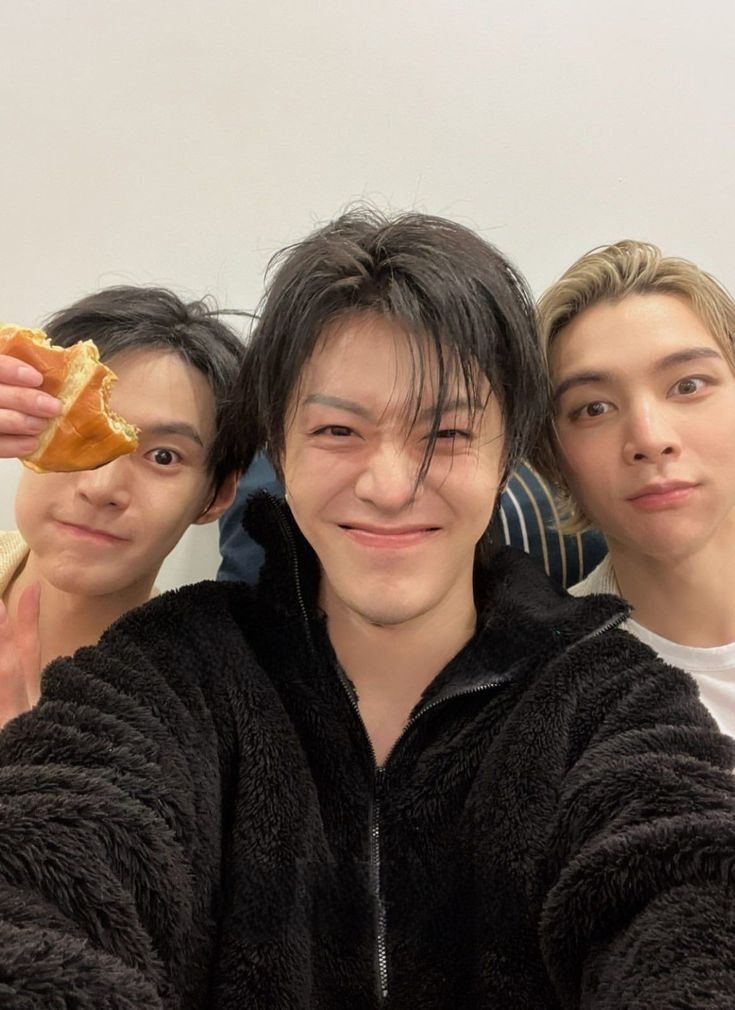 three young men posing for the camera with food in front of their eyes and one holding a hot dog up to his eye